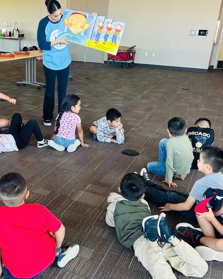 Children sitting in a circle on the floor while an instructor holds up a picture book