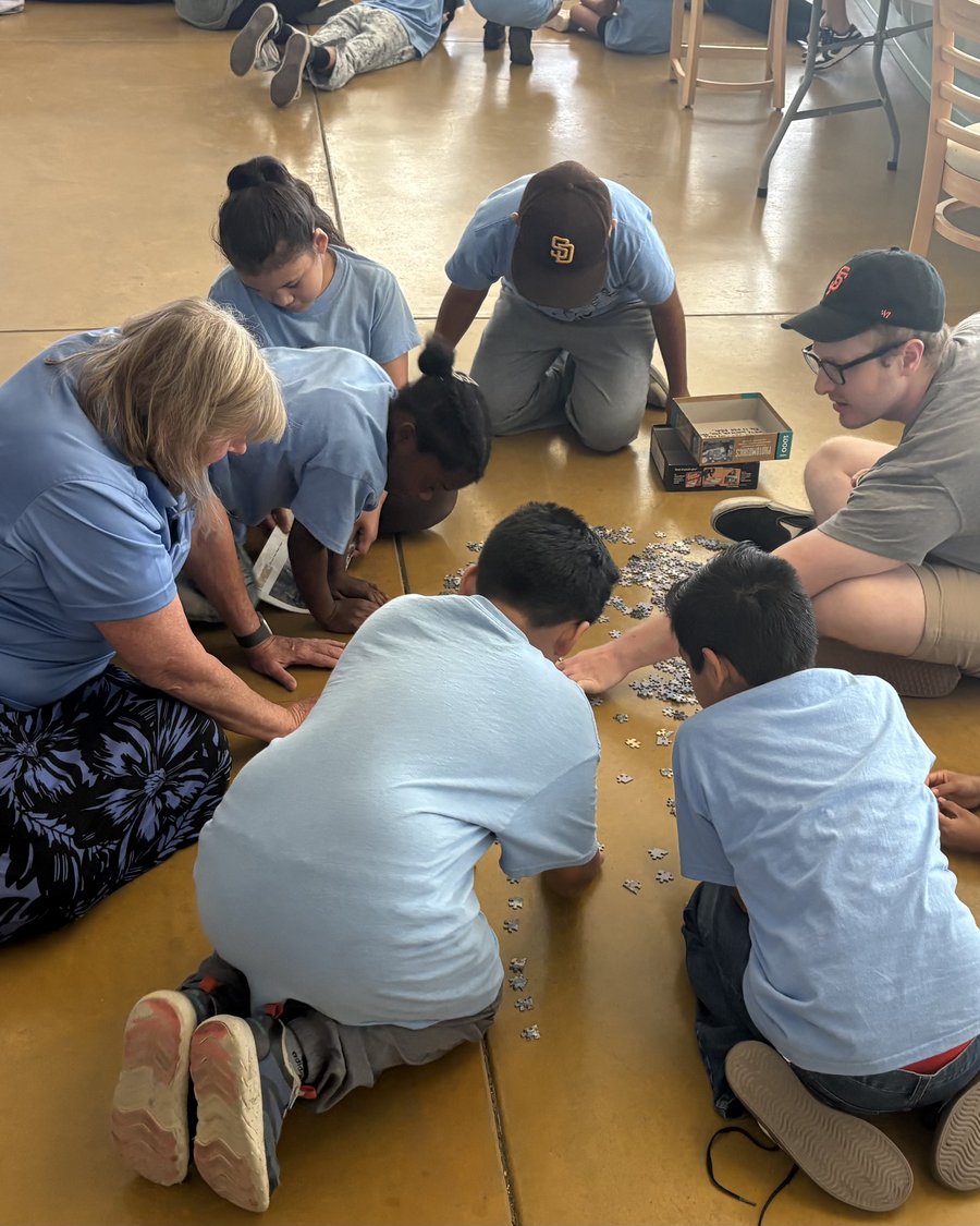 Volunteers and students of all ages lying on the floor together, working on a jigsaw puzzle at the Learning Academy