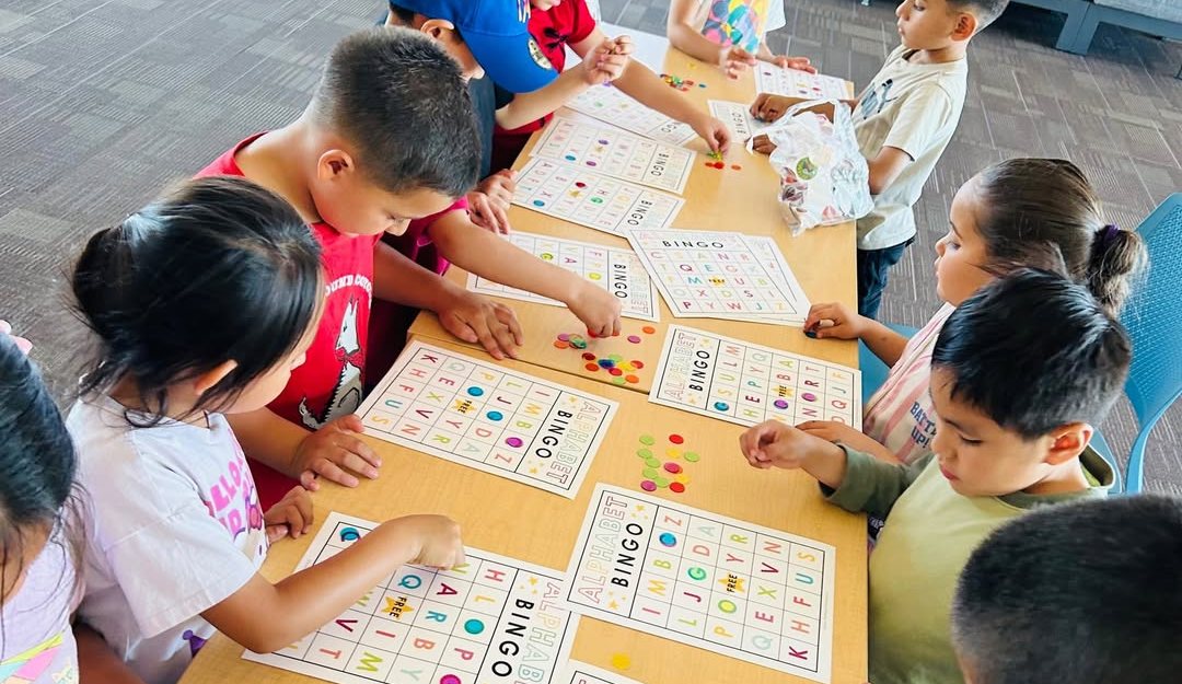 Young children around a long table playing a letter-recognition bingo game